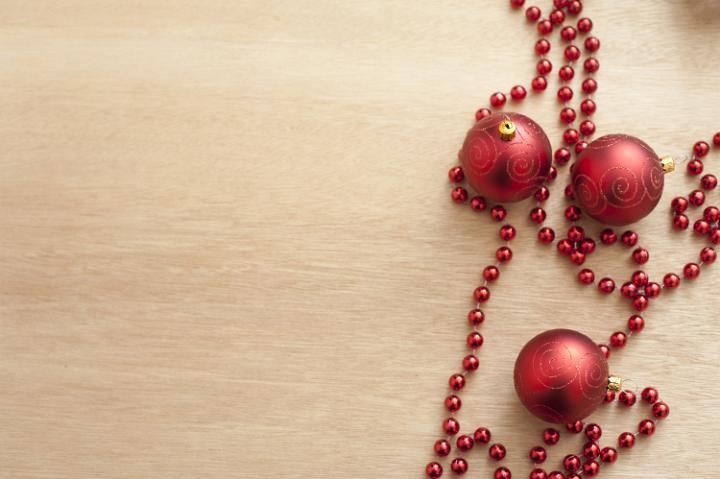 Red tree decoration and red garland lying on wooden light brown table. From above