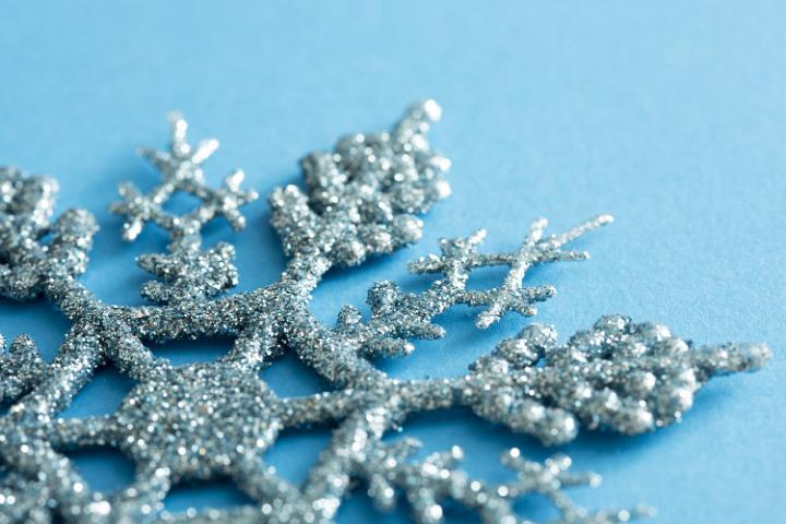 Glitter texture on a blue snowflake Christmas decoration in a close up oblique view on a matching cool blue winter background with copy space