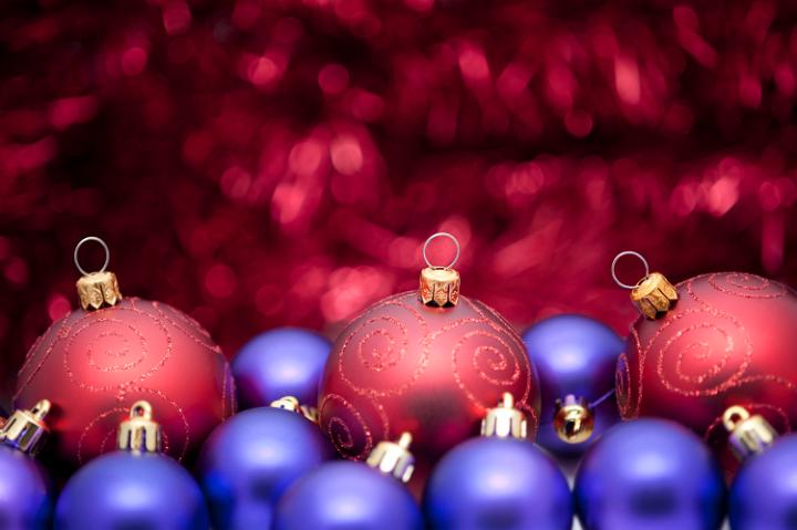 a sumptuous red and purple coloured christmas background, baubles in the foreground and defuse tinsel covering an area of text to the rear