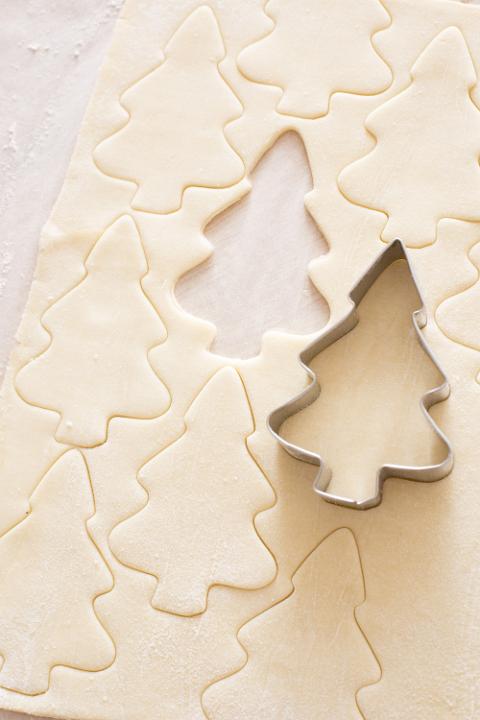 Close up of a sheet of dough with a cutter in shape of a christmas tree