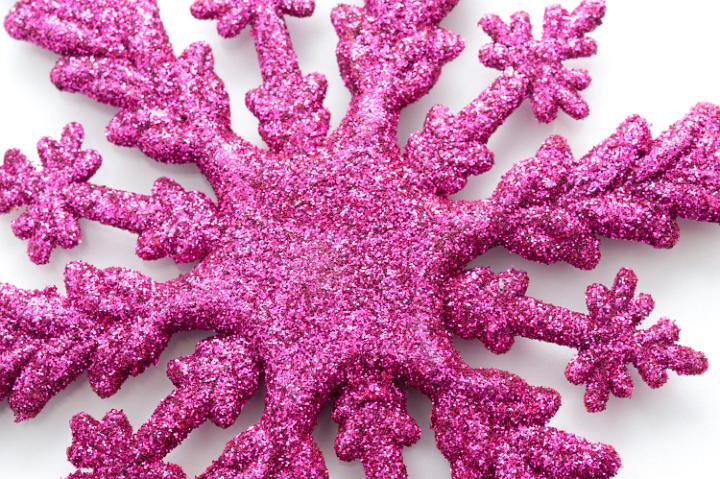 Closeup of a textured deep pink Christmas snowflake ornament with a glitter surface on a white background