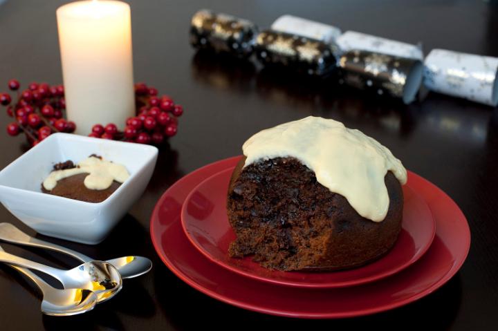Delicious traditional Christmas pudding with a rich fruity texture topped with brandy sauce and served on a festive Christmas table
