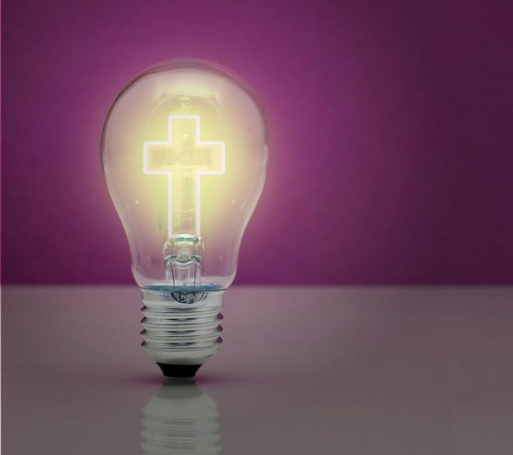 Conceptual image of strong religious faith at Christmas with the cross of Christ burning brightly inside a light bulb with copyspace