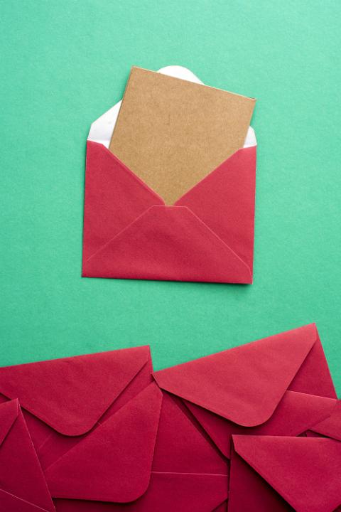 Blank card in festive red Christmas envelope protruding from the open flap with a bottom border of additional stationery over green with copy space for your seasonal greeting