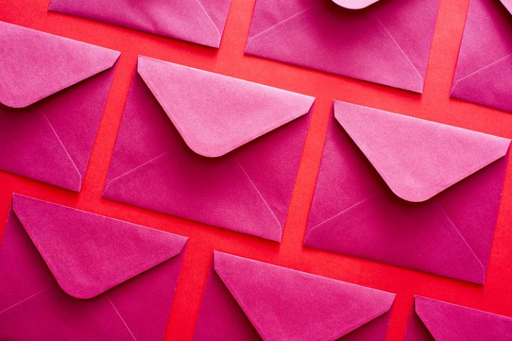 Pink opened envelopes lying in rows on red surface.