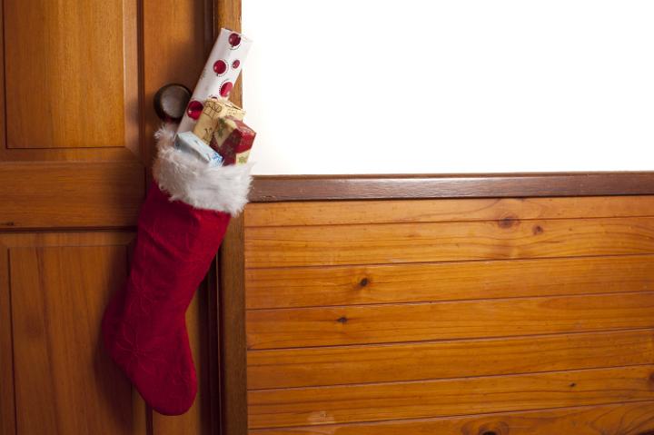 Colorful festive red Christmas stocking filled with gifts hanging on a wooden interior house door to celebrate the holiday season