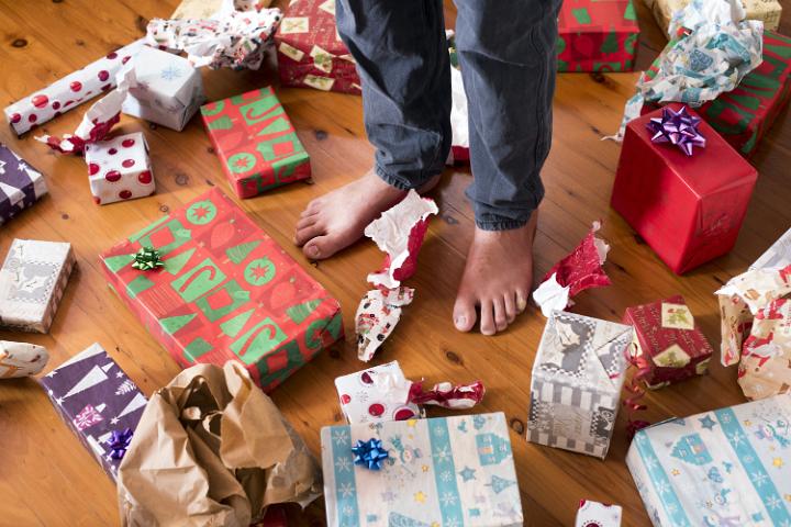 Barefoot man standing amongst unwrapped gifts on a wooden floor on Christmas morning in a holiday concept