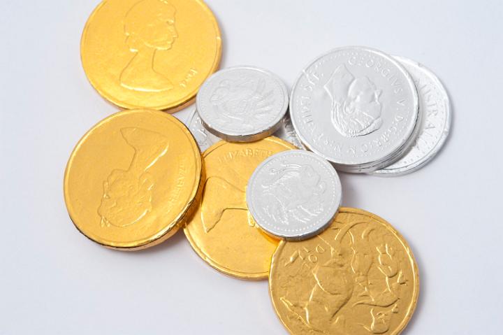 Collection of foil wrapped shiny metallic gold and silver chocolate coins scattered randomly on a white background, high angle view