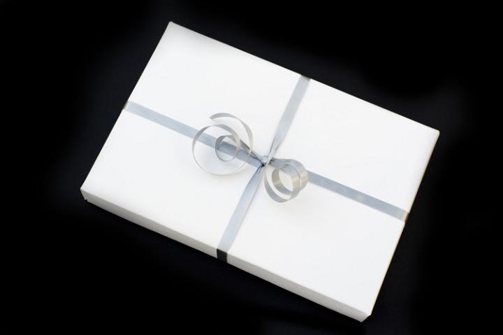 a white wrapped christmas gift with a silver bow against a black backdrop