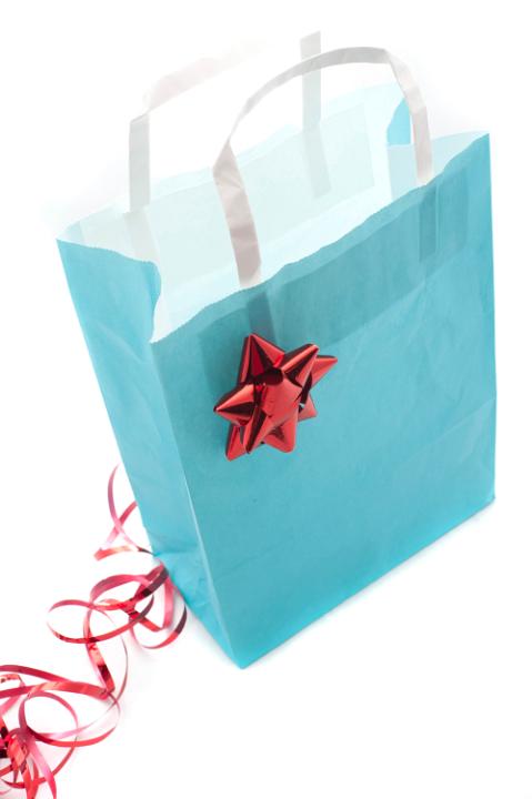 Close up of a blue paper Christmas shopping bag decorated with an ornate festive red ribbon and bow, high angle view on a white background