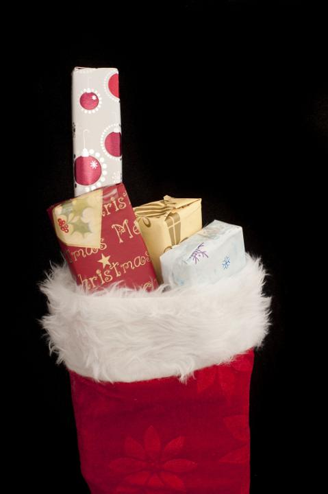 Small Christmas gifts filling a festive red stocking over a black background with copy space for your holiday greeting