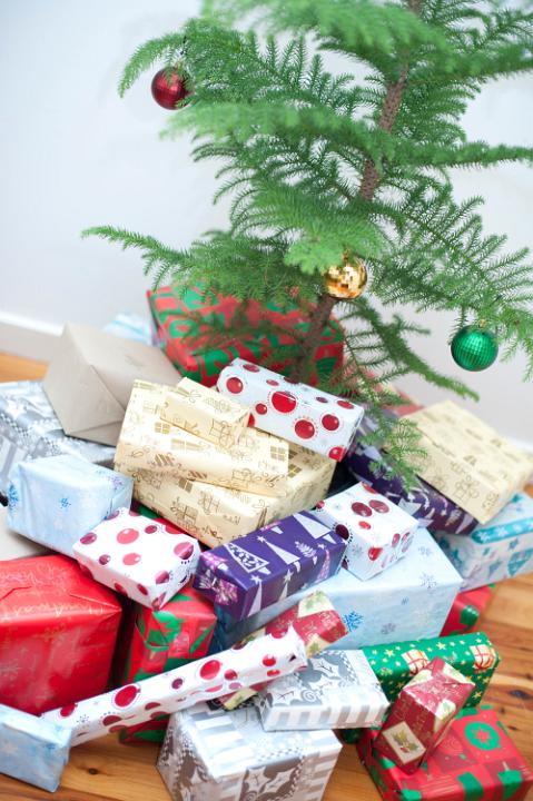 Small simple evergreen Christmas tree and a pile of gifts wrapped in traditional colourful patterned gift-wrap in a variety of shapes and sizes
