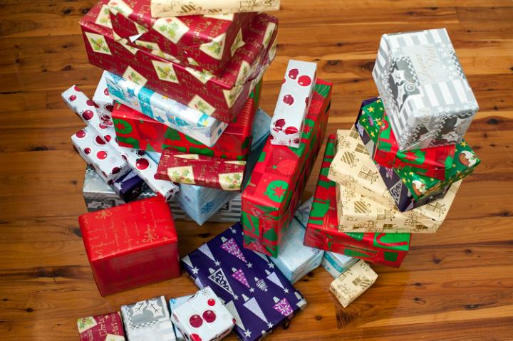 High angle view of a festive collection of Christmas gifts in colourful patterned gift-wrap stacked on a hardwood floor in a living room of a house