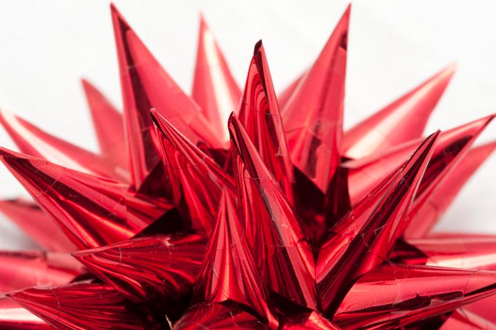 Closeup of a shiny ornamental red spiky Christmas bow on a white background