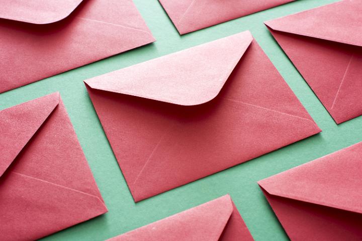 Red festive envelope background arranged in rows over green in a holiday greetings concept, close up full frame view