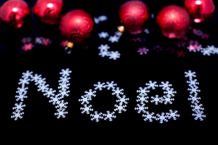 Noel greeting card with text in tiny snowflakes and colourful red Christmas baubles on a dark background