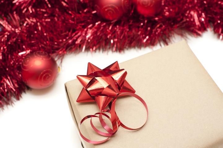 Plain brown gift decorated with a decorative festive red Christmas bow on a white background with border of tinsel and baubles