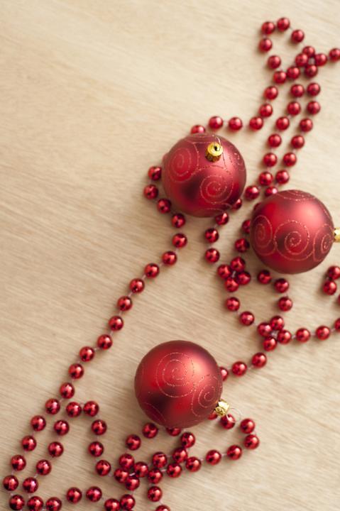 Close-up of three red Christmas balls and red beads on wooden table