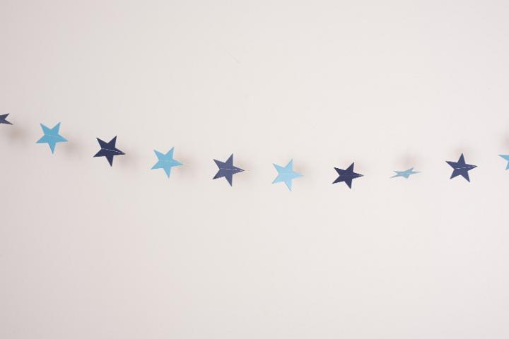 Delicate chain of small blue Christmas stars strung across a white background with copy space for your seasonal greeting