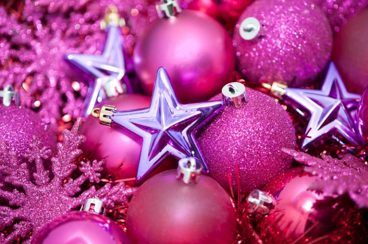a festive holiday background with pink coloured glittery christmas tree ornaments on a bed of sparkling tinsel