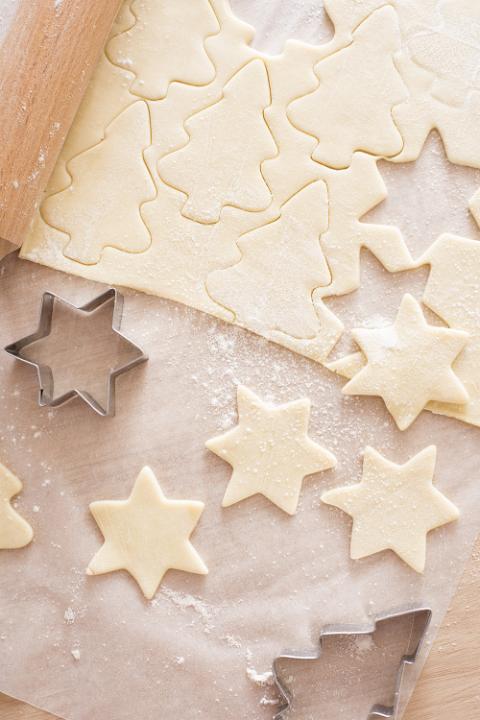 Preparing traditional Christmas star cookies with cut out pastry shapes and cookie cutters on oven paper viewed from above