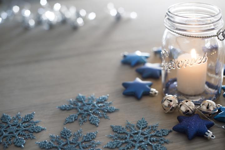 Festive blue themed Christmas party table with a burning candle in a glass jar surrounded by decorations with sparkling lights in the background