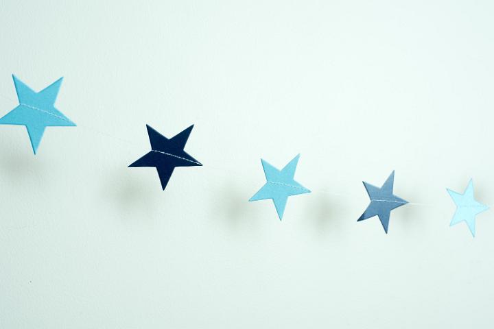 Diagonal string of blue paper stars on a pale blue background with copy space for your Christmas or festive greeting