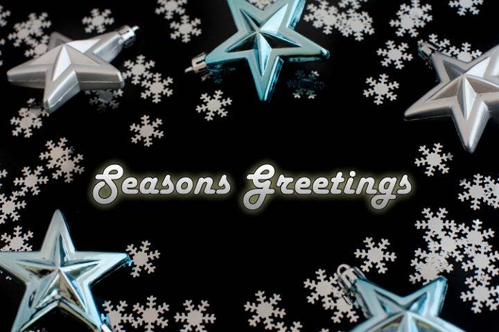 Seasons greetings card with glowing text surrounded by snowflakes and stars on a black background