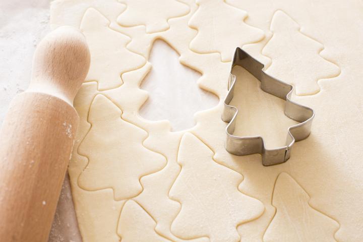 Baking tree shaped Christmas cookies at home with a metal cookie cutter, rolling pin and cut out shape on neatly rolled and trimmed dough