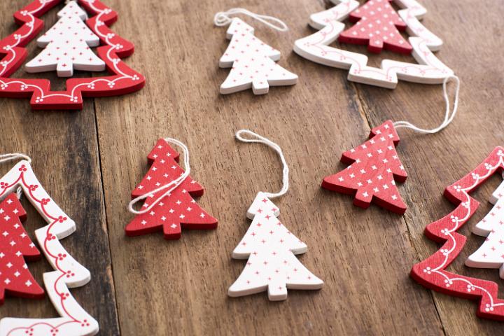 Wooden tree shaped Christmas ornaments with a decorative red and white pattern lying on a wooden table in a full frame view