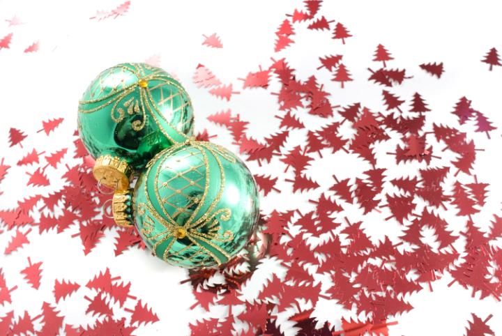 a festive background of red tree shaped confetti and two green reflective baubles