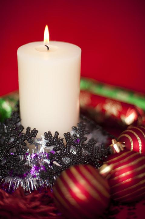 an arrangement of a burning christmas candle and various sparkling christmas decorations pictured with a narrow depth of field