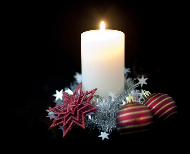 a soft focus candle and flame surrounded by christmas ornaments and tinsel
