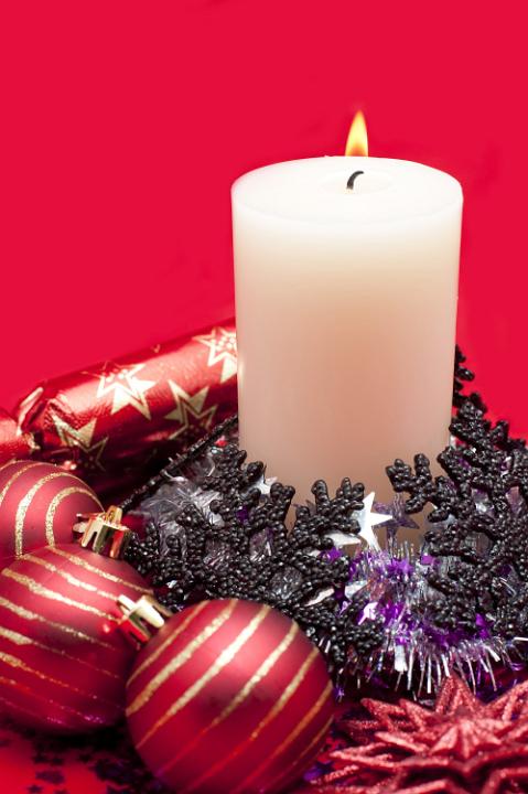 an arrangement of a lit christmas candle and various sparkling christmas decoration including baubles and tinsel