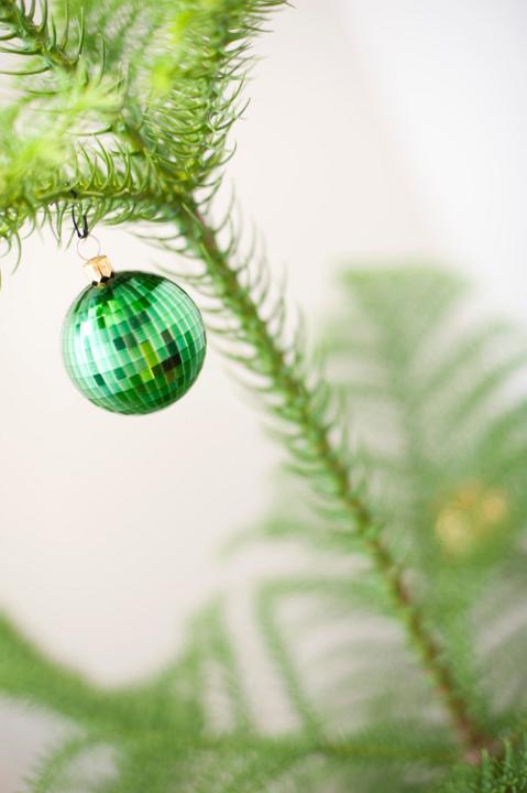 Close-up of an ornamental shiny green bauble hanging on the branch of a Christmas tree, symbol of joy