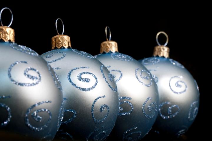 A receding row of pretty silvery blue Christmas balls decorated with glitter curlicues on a dark background