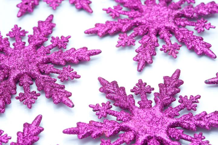 Pink snowflake ornaments with textured glitter surfaces scattered on a white background to celebrate the festive season