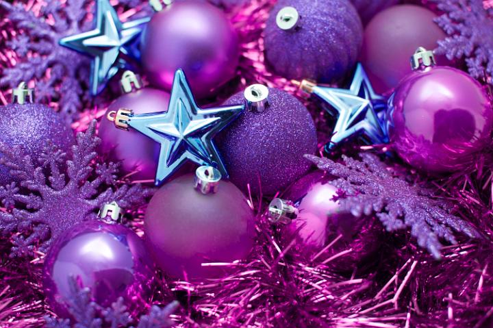 An assortment of different purple and pink Christmas decorations including baubles, snowflakes, stars and tinsel
