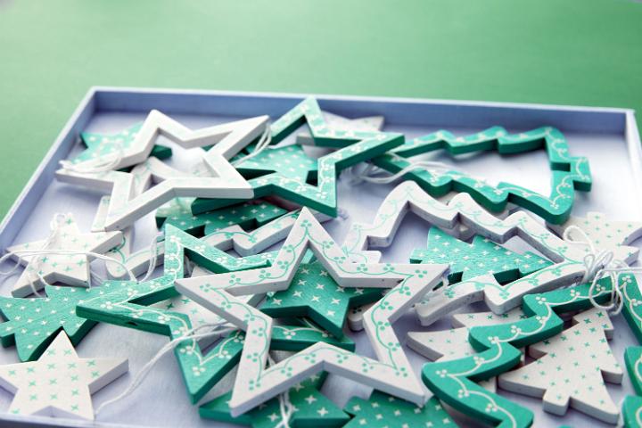 Tray of wooden green star and tree-shaped ornaments for hanging on the Christmas tree over a green background
