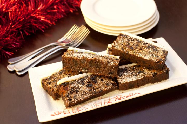 Slices of rich spicy Christmas fruit cake with raisins and dried fruit and topped with a marzipan and almond paste icing on a plate on a festive seasonal table