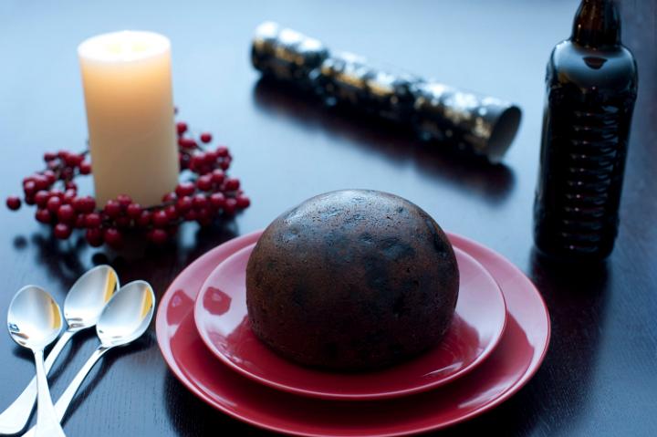 Traditional rich fruity Christmas pudding served at the table on two red plates waiting to be flamed with brandy for a festive celebration
