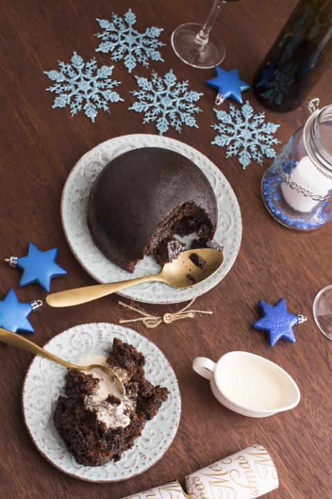 Eating homemade fruity Christmas pudding topped with brandy cream served on a festive table with blue decorations, viewed from above