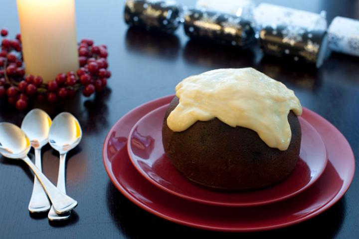 A small traditional steamed fruity Christmas pudding topped with brandy custard and served for dessert on a festive table