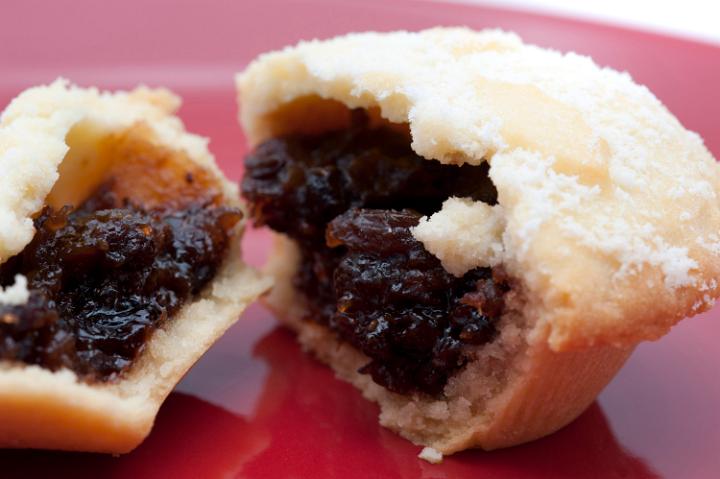 Close up detail of a fruity mince pie with a freshly baked golden pastry crust broken open to reveal the spicy fruit filling rich in raisins