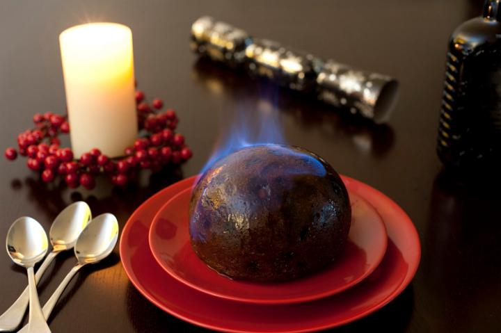 Traditional rich fruity flaming brandy pudding served for a delicious Christmas dessert on festive red plates standing on a table with a glowing seasonal candle