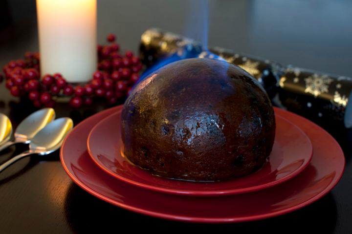 Flaming traditional fruity Christmas pudding set alight with brandy before serving on a festive Xmas table for dinner