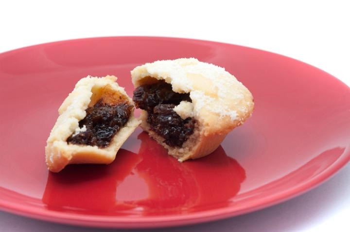 Homemade delicious traditional Christmas mince pie with a rich fruity filling and golden crust broken open on a festive red plate