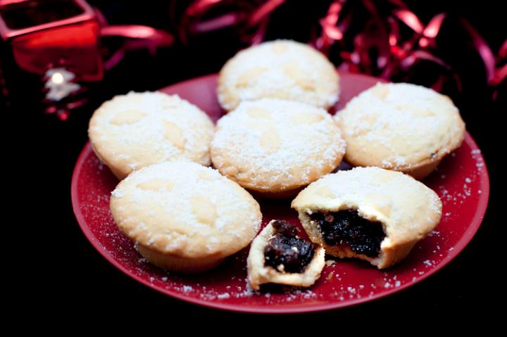 Plate of freshly baked festive Christmas mince pies with decorated golden crusts and spicy fruit filling served sprinkled with sugar, one broken open to reveal the filling