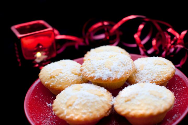 Plate of Christmas mince pies with golden crusts and fruity filling sprinkled with sugar and served on a red plate on a festive table with decorations
