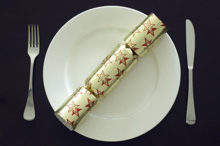 a place setting at a christmas dinner table, plate, knife, fork and a christmas cracker